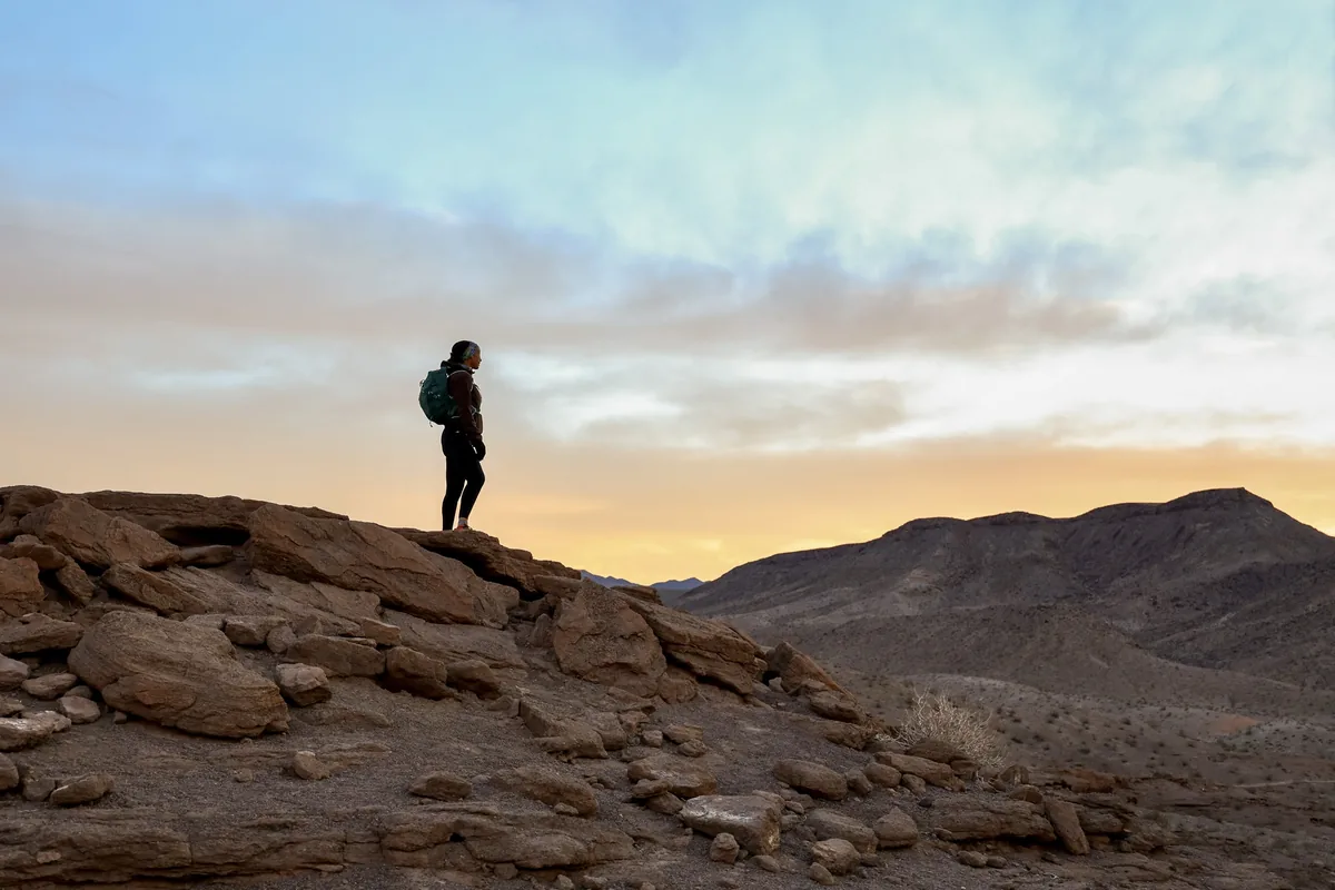 Hiker standing on a desert ridge under a sunset sky
