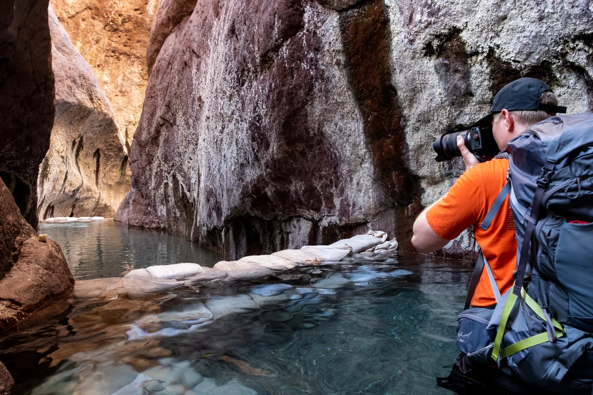 Kyle Barton in an orange shirt photographing a pool in a slot canyon