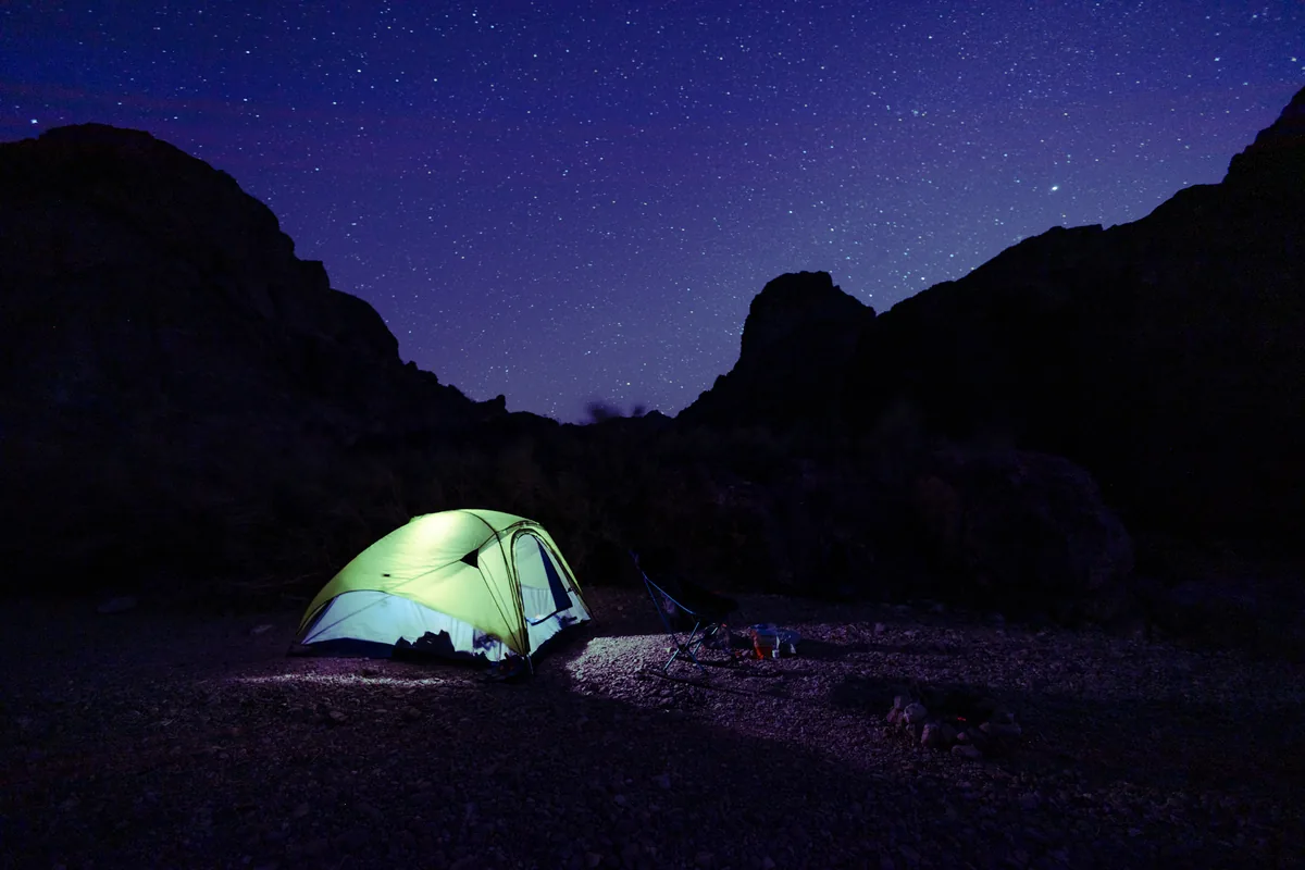 Single glowing green tent under a starry sky in a desert canyon
