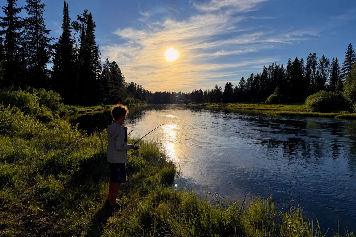 Young angler fishing a river at sunset, seen from behind